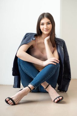 Beyaz arka planda kot pantolon ve ceket giyen genç bir kadın.