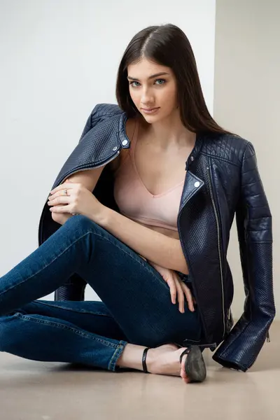 Beyaz arka planda kot pantolon ve ceket giyen genç bir kadın.