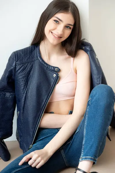 Beyaz arka planda kot pantolon ve ceket giyen genç bir kadın.