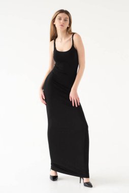 Siyah elbiseli güzel bir kızın uzun bir portresi. Beyaz stüdyo arka planında gülümsüyor. Kameraya bakıyorum..