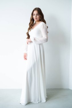 Stüdyoda poz veren beyaz elbiseli güzel bir genç kadının tam boy fotoğrafı.