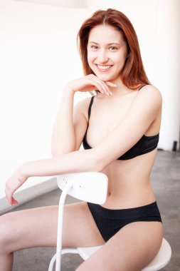 Odada sandalyede oturan iç çamaşırlı genç bir kadının portresi.