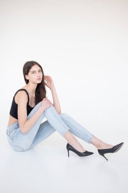 Siyah kot ve beyaz tişörtlü güzel bir kadın stüdyoda poz veriyor. Beyaz arka planda izole edilmiş.