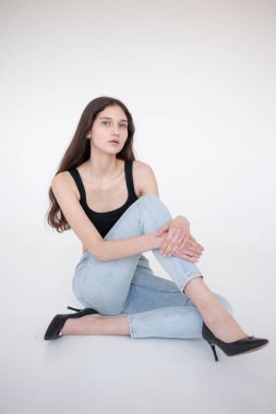 Siyah kotlu, beyaz bluzlu, yerde oturan ve kameraya poz veren güzel bir kadın. Stüdyo çekimi.