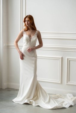 Güzel, genç bir gelin, uzun saçlı, beyaz dantelli bir elbise içinde, gülümsüyor.