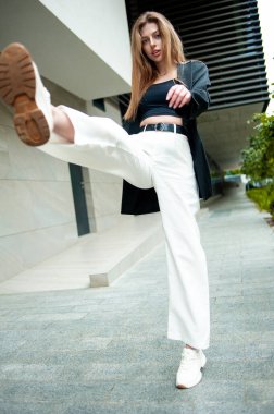 Beyaz gömlekli ve pantolonlu güzel bir kız sokakta poz veriyor..