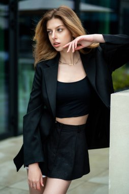 Siyah elbiseli genç kız arka planda poz veriyor.