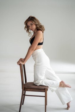 Beyaz elbiseli genç kız gri arka planda poz veriyor, modern bir vücut ve kaslı spor figürü..