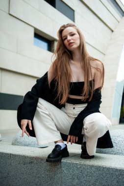Genç, güzel, uzun saçlı, şehirde şık bir siyah ceketle poz veren bir manken.
