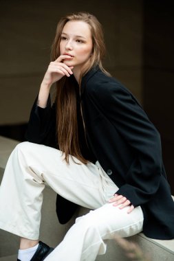 Beyaz gömlekli ve siyah pantolonlu güzel kız merdivenlerde oturuyor.