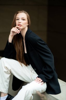 Modern bir binada merdivenlerde oturan genç bir kadın. Gündelik giysiler içinde genç bir kadının portresi. Güzel kadın model.