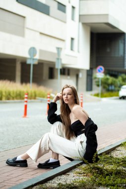 Genç bir kadın cep telefonuyla sokakta oturuyor.