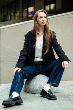 Şehir parkındaki merdivenlerde oturan uzun saçlı genç bir kadın.