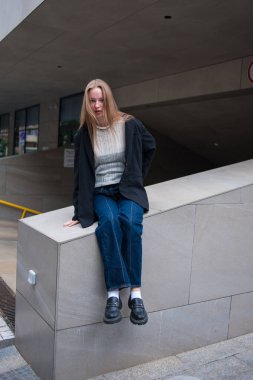 Sarışın ve mavi gözlü genç kız, şehirde bir bankta oturuyor..