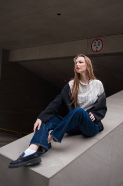 Gri kazaklı ve kot pantolonlu genç kız şehirde poz veriyor.