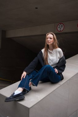 Siyah ceketli ve gri kotlu bir kız taş bir merdivende oturuyor. bir kızın konsepti ve modern moda.