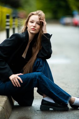 Siyah gömlekli ve kot pantolonlu güzel genç bir kız bir yaz günü parkta oturur..