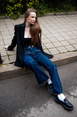 Siyah ceketli, uzun siyah saçlı genç ve güzel bir kız şehrin eski duvarının yanında poz veriyor.