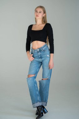 Stüdyoda beyaz arka planda siyah saçlı, kot pantolonlu genç bir kadın.