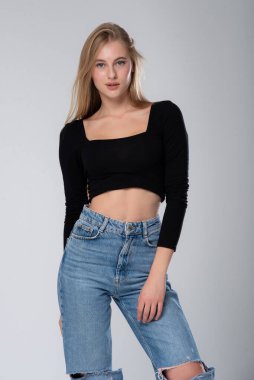 Kot pantolonlu güzel bir kadın ve siyah arka planda beyaz bir bluz. Stüdyo çekimi.