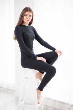 Beyaz elbiseli güzel bir kadın siyah stüdyoda duvarda poz veriyor.