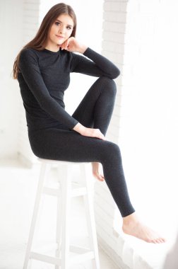 Siyah takım elbiseli, uzun siyah kıvırcık saçlı genç ve güzel bir kız bir odada bir sandalyede oturuyor..