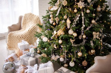 Elegant Christmas interior with a decorated tree in gold and white, wrapped gifts, a vintage beige sofa, and an armchair with a cozy knit blanket. Bright white walls create a festive, minimalist ambiance clipart