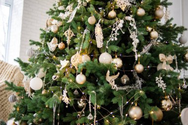 Süslü, altın ve beyaz bir ağaç, sarılı hediyeler, klasik bej bir kanepe ve rahat örgü battaniyeli bir koltuk. Parlak beyaz duvarlar şenlikli, minimalist bir ortam yaratır.