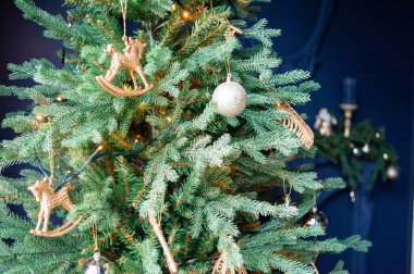 Süslü, altın ve beyaz bir ağaç, sarılı hediyeler, klasik bej bir kanepe ve rahat örgü battaniyeli bir koltuk. Parlak beyaz duvarlar şenlikli, minimalist bir ortam yaratır.