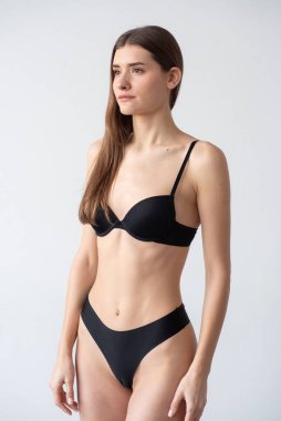 Stüdyoda poz veren siyah mayo giymiş genç bir kadın.