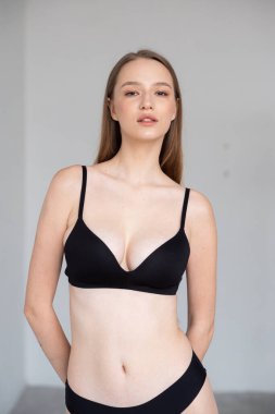 Beyaz arka planda siyah iç çamaşırlarıyla poz veren güzel bir kızın portresi.