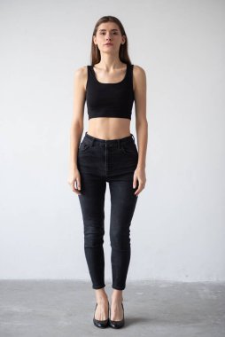 Uzun kahverengi saçlı ve kot pantolonlu güzel bir kadının tam boy portresi.