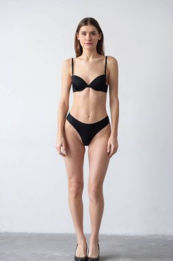 Beyaz duvar arkasında bikinili güzel, zayıf bir kadın.