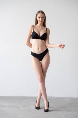 Gri arka planda duran iç çamaşırlı çekici genç bir kızın tam boy portresi.