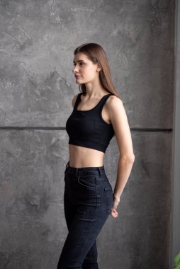 Çatı katı tarzında duvarın yanında poz veren kot pantolonlu genç bir kadın.