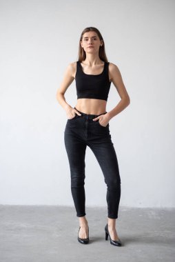 Stüdyoda gri arka planda siyah pantolonlu ve beyaz gömlekli genç bir kadın..