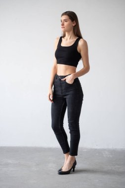 Siyah bluzlu genç bir kadın ve gri arka planda duran kot pantolonlar.