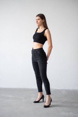 Siyah bluz ve beyaz arka planda pantolon giyen güzel bir kız.