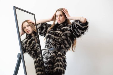 fashionable woman poses in a black and white faux fur coat with a bold pattern, wearing a black lingerie-style top. Her long, straight, light brown hair and confident expression add to the chic, edgy look clipart