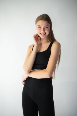 Beyaz arka planda siyah takım elbiseli, uzun sarı saçlı, gülümseyen kadın modelin portresi..