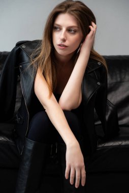 Stüdyoda beyaz bir arka planda siyah elbiseli ve deri ayakkabılı genç bir kadın..