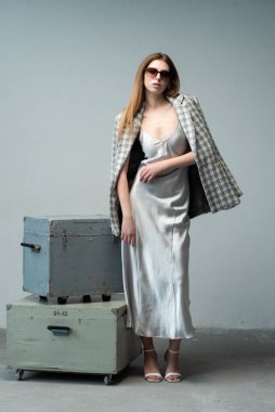 Gri bir arka planda bavulu olan güzel genç bir kadın..