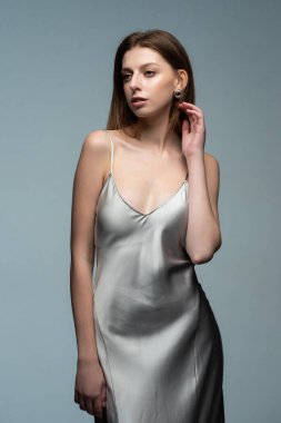 Gri bir arka planı olan beyaz elbiseli genç bir kadın..