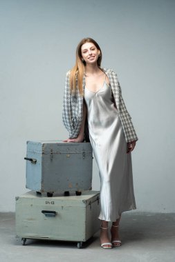 Gri arka planda büyük bir bavulu olan güzel bir kadın.