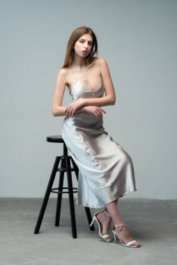 Beyaz elbiseli kadın gri arka planda poz veriyor.