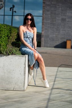 Kotlu uzun saçlı, beyaz tişörtlü, yaz şehrinde merdivenlerde oturan güzel bir esmerin portresi..