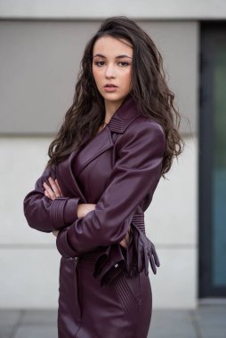 Siyah ceketli esmer kadın, uzun saçlı modern binanın önünde poz veriyor..