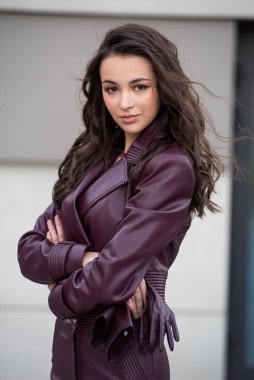 Uzun kahverengi kıvırcık saçlı, siyah ceketli güzel bir kadın şehirde poz veriyor.