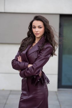 Siyah ceketli esmer kız ofis binasının yanında duruyor.