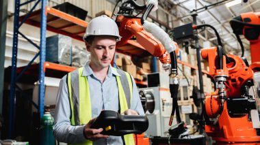 Industrial engineers control the automatic arms machine welding robotics in industrial manufacturing factories.